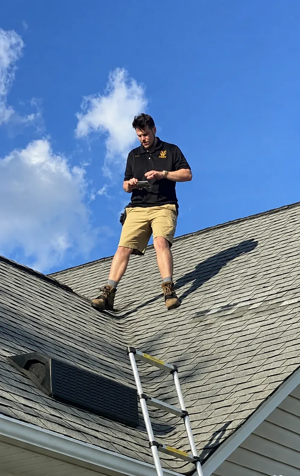 Austin documenting a roof inspection from the ridge with his phone