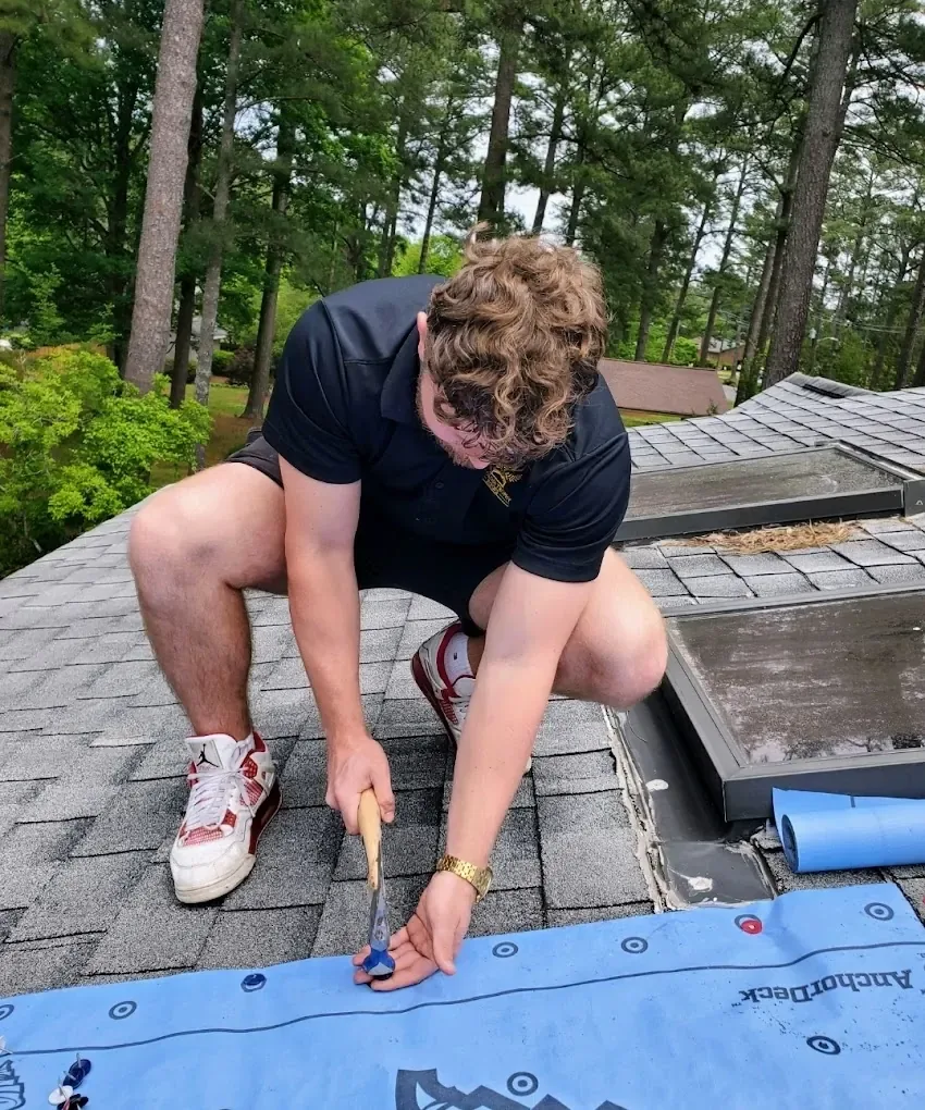 Carolina Trophy Roofs crew member fastening a reinforced emergency tarp over a storm-damaged roof section beside the skylights
