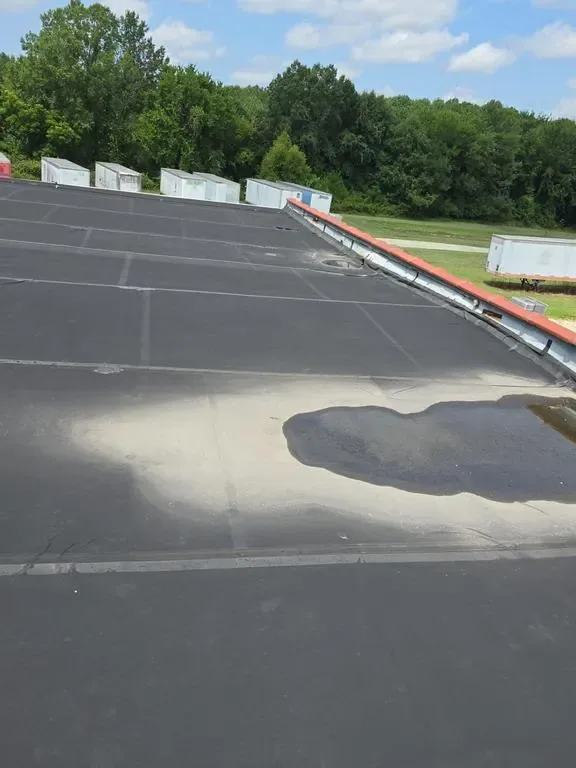 Ponding stain across a black membrane commercial flat roof beside rooftop HVAC equipment