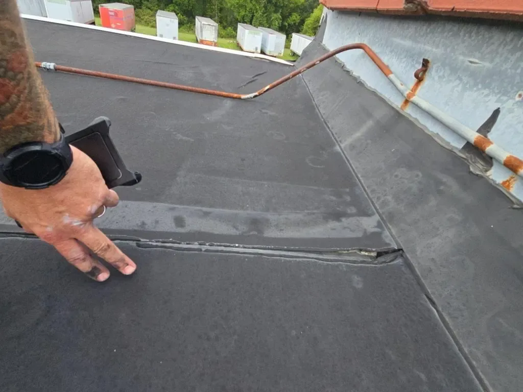 Inspector pointing out a failing seam on a commercial rubber roof during a pre-coating assessment