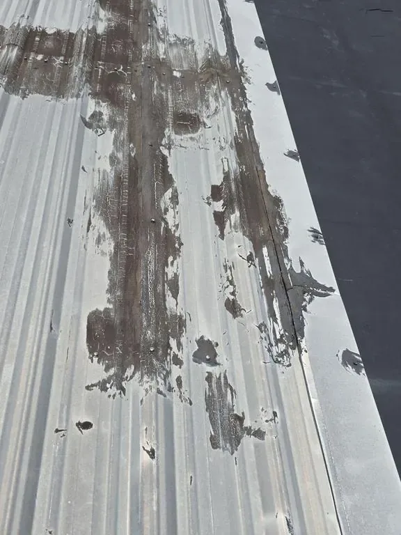 Weathered metal roof panels streaked with failed mastic and peeling coating before restoration