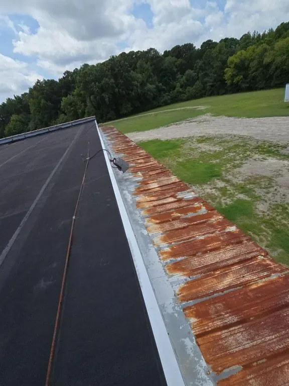 Heavily rusted metal roof panels along a flat roof edge before restoration