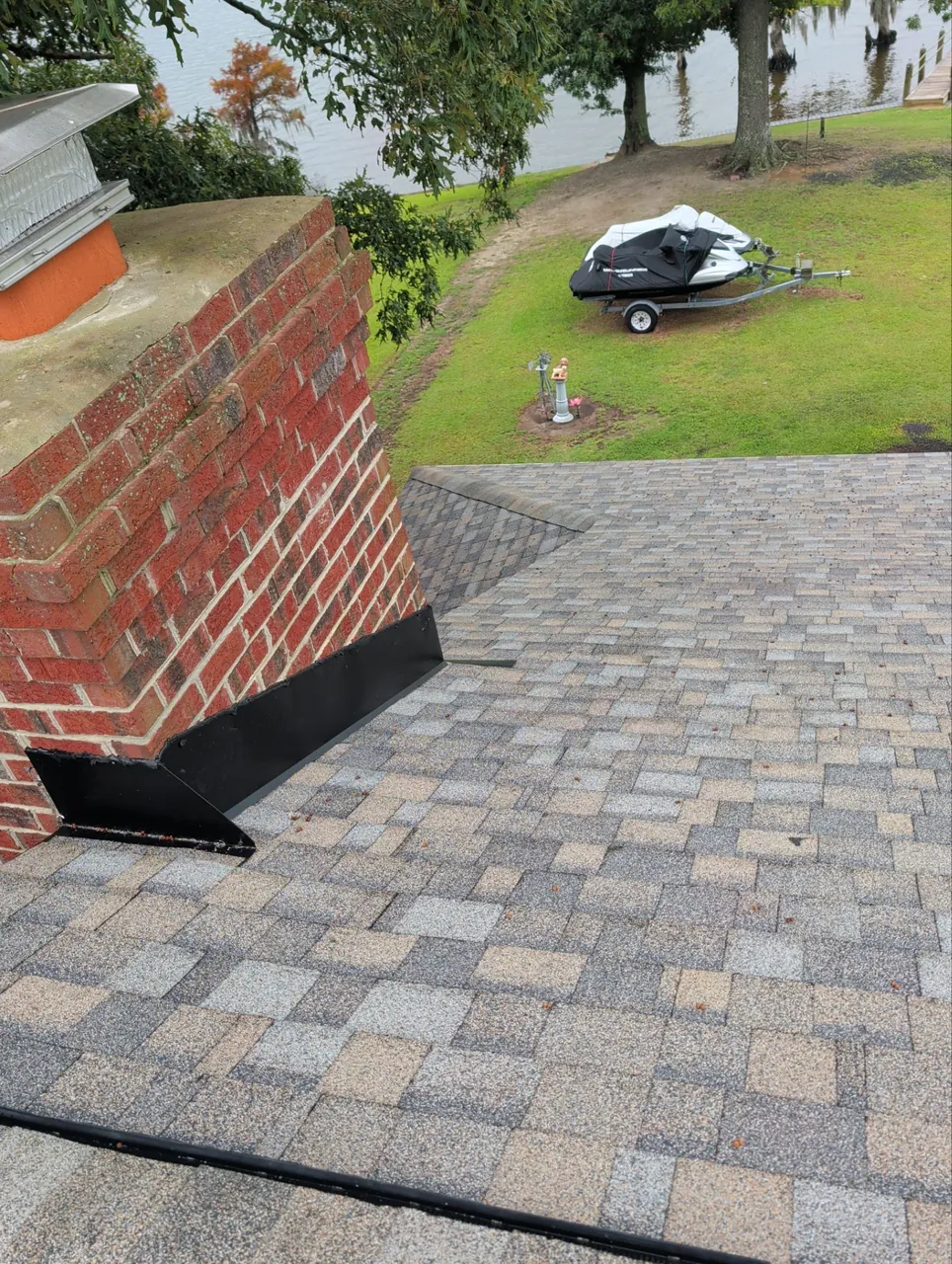 New black flashing at a brick chimney in a new architectural shingle roof in Winfall, NC