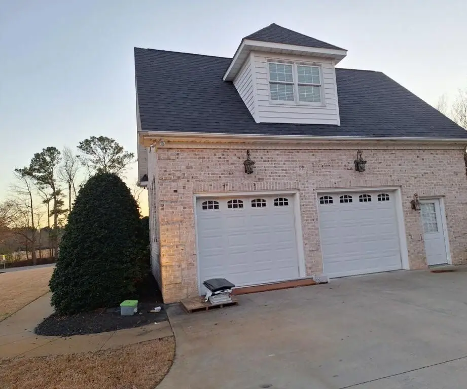Brick garage wing with a dormer and a new charcoal shingle roof at dusk in Goldsboro, NC