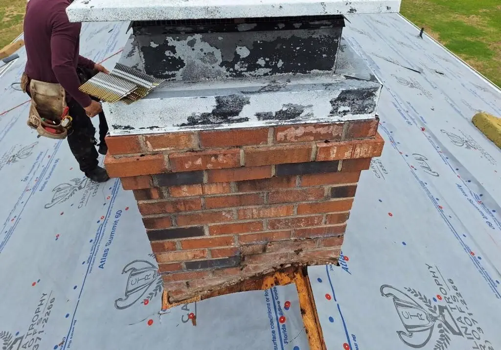 Roofer at a brick chimney on a roof covered in Atlas Summit 60 synthetic underlayment printed with the Carolina Trophy Roofs logo, Goldsboro, NC