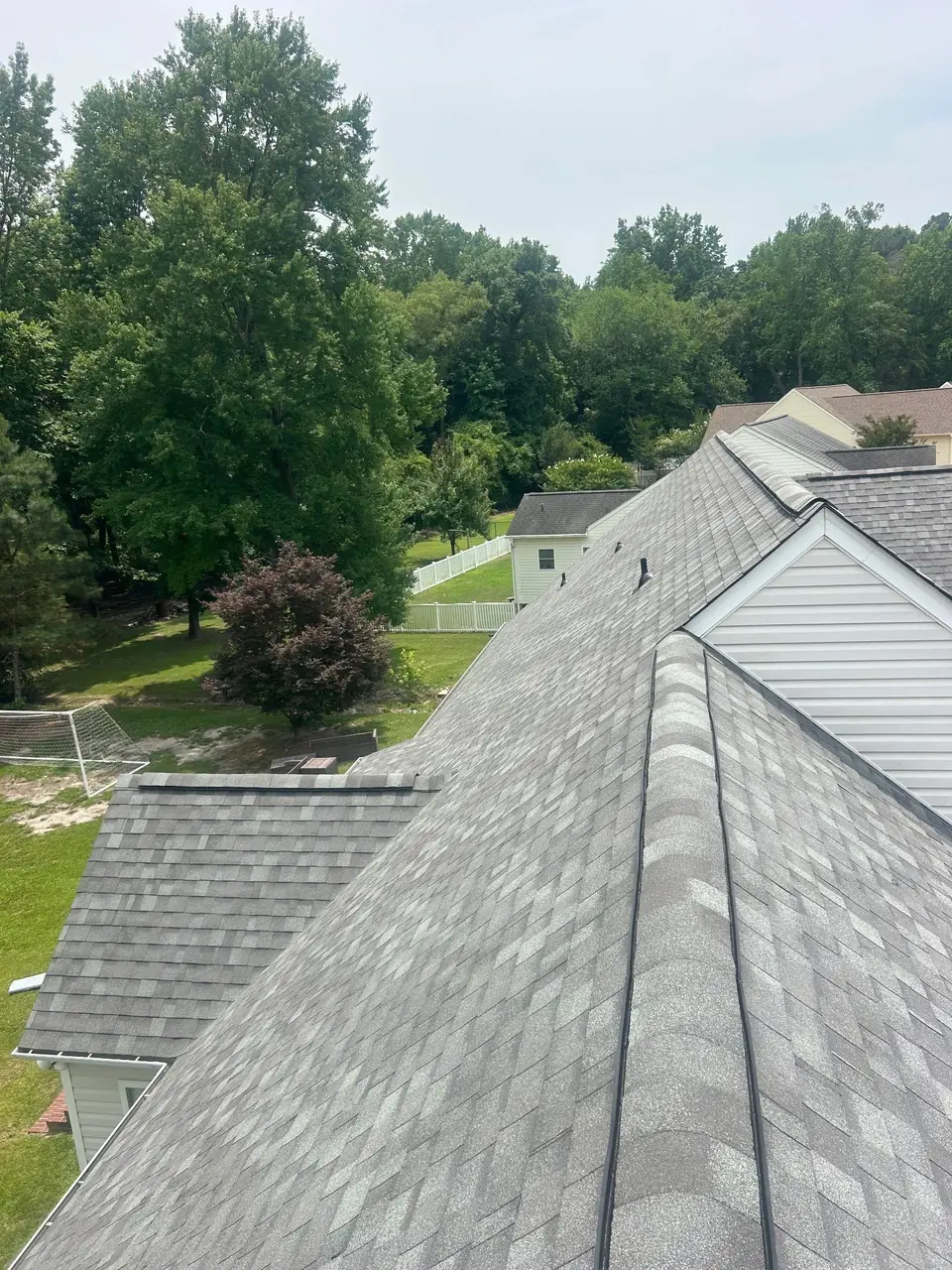 New light gray shingles with hip and ridge caps on a roof in Goldsboro, NC, looking over the back yard