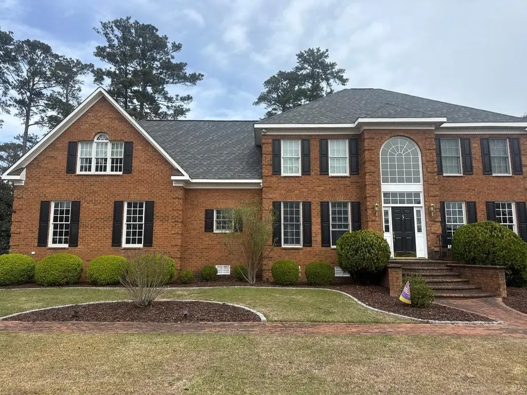 Two-story brick colonial in Greenville, NC with a charcoal architectural shingle roof, black shutters and an arched window