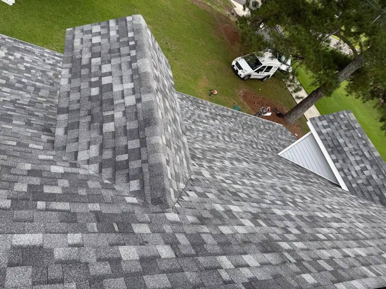 Shingle-clad chimney chase rising from a new gray architectural shingle roof in Greenville, NC, beside a dormer valley