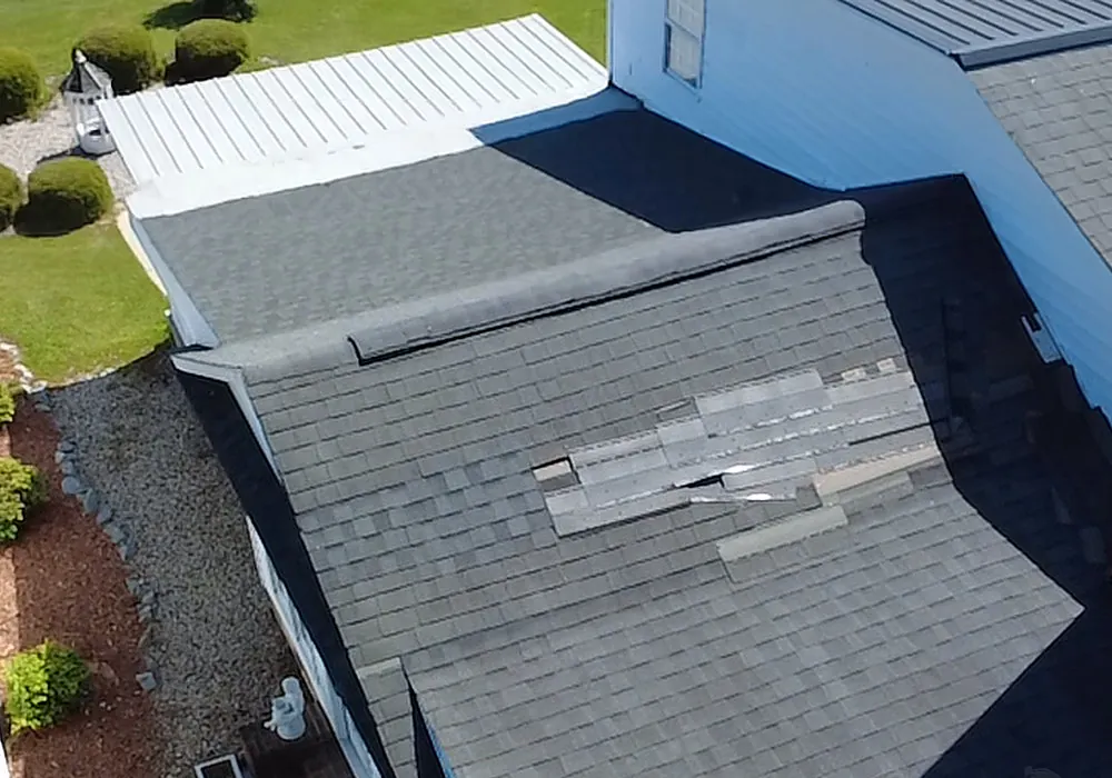 Aerial view of a lower shingle roof section on a white home in Grimesland, NC with a patch of missing and displaced shingles