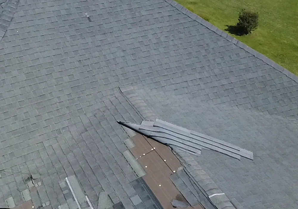 Close aerial view of torn and missing asphalt shingle tabs along a hip in Grimesland, NC, with the layers beneath exposed