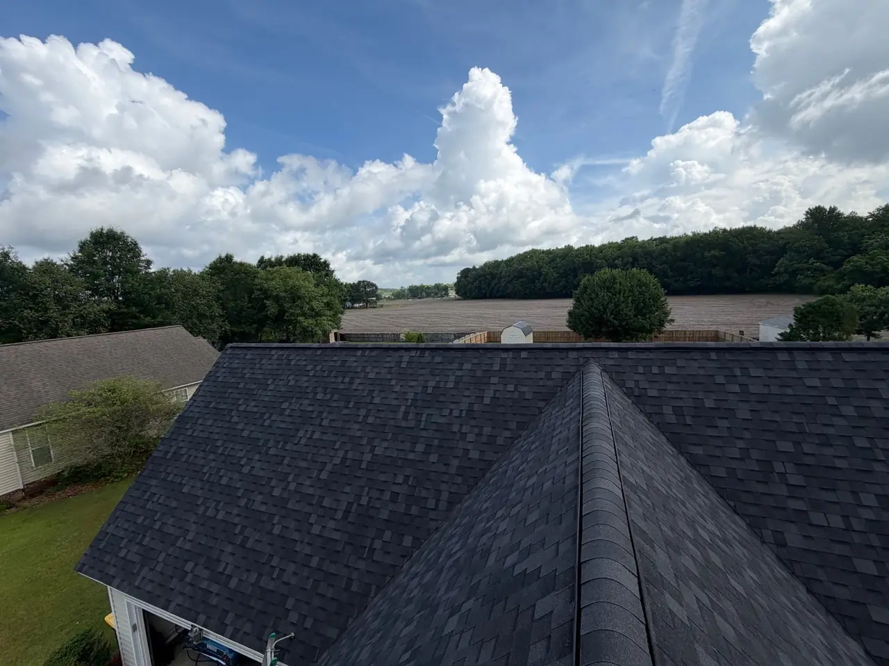 Finished charcoal architectural shingle roof in Winterville, NC, seen from the ridge under a summer sky