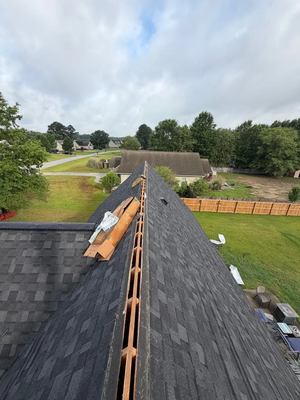 Ridge vent being installed along the peak of a new charcoal shingle roof in Winterville, NC, cap shingles staged beside it