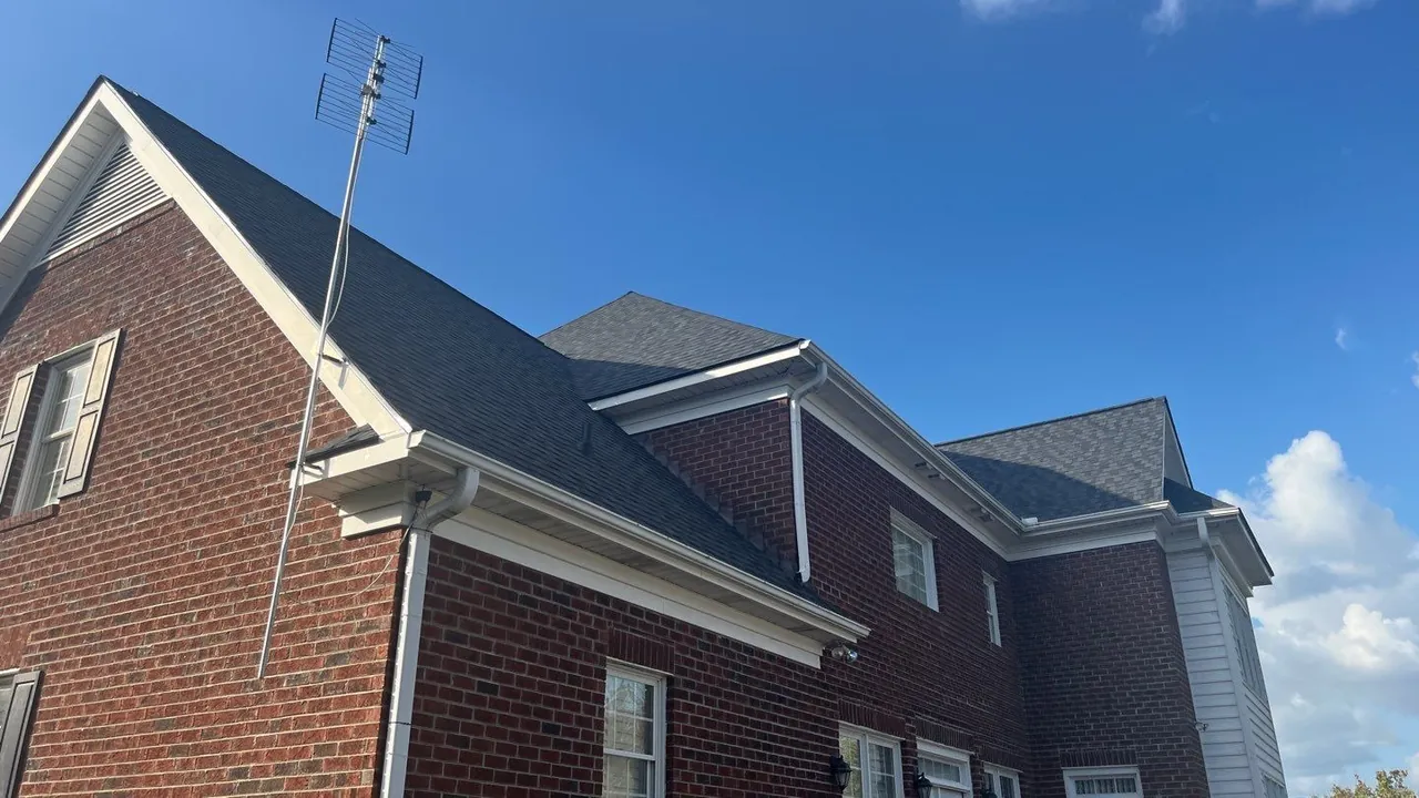Two-story brick home in Kinston, NC with a new charcoal architectural shingle roof under a blue sky