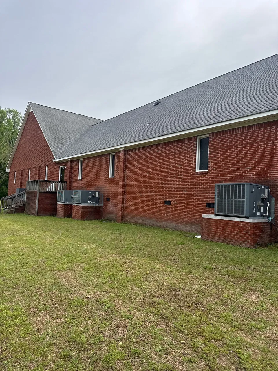 Gable end and long rear slope of a red-brick building with a new gray shingle roof in Snow Hill, NC