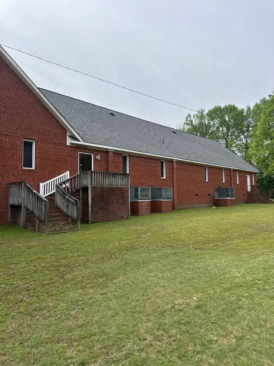 Long red-brick building in Snow Hill, NC with a new gray architectural shingle roof, seen from the back lawn
