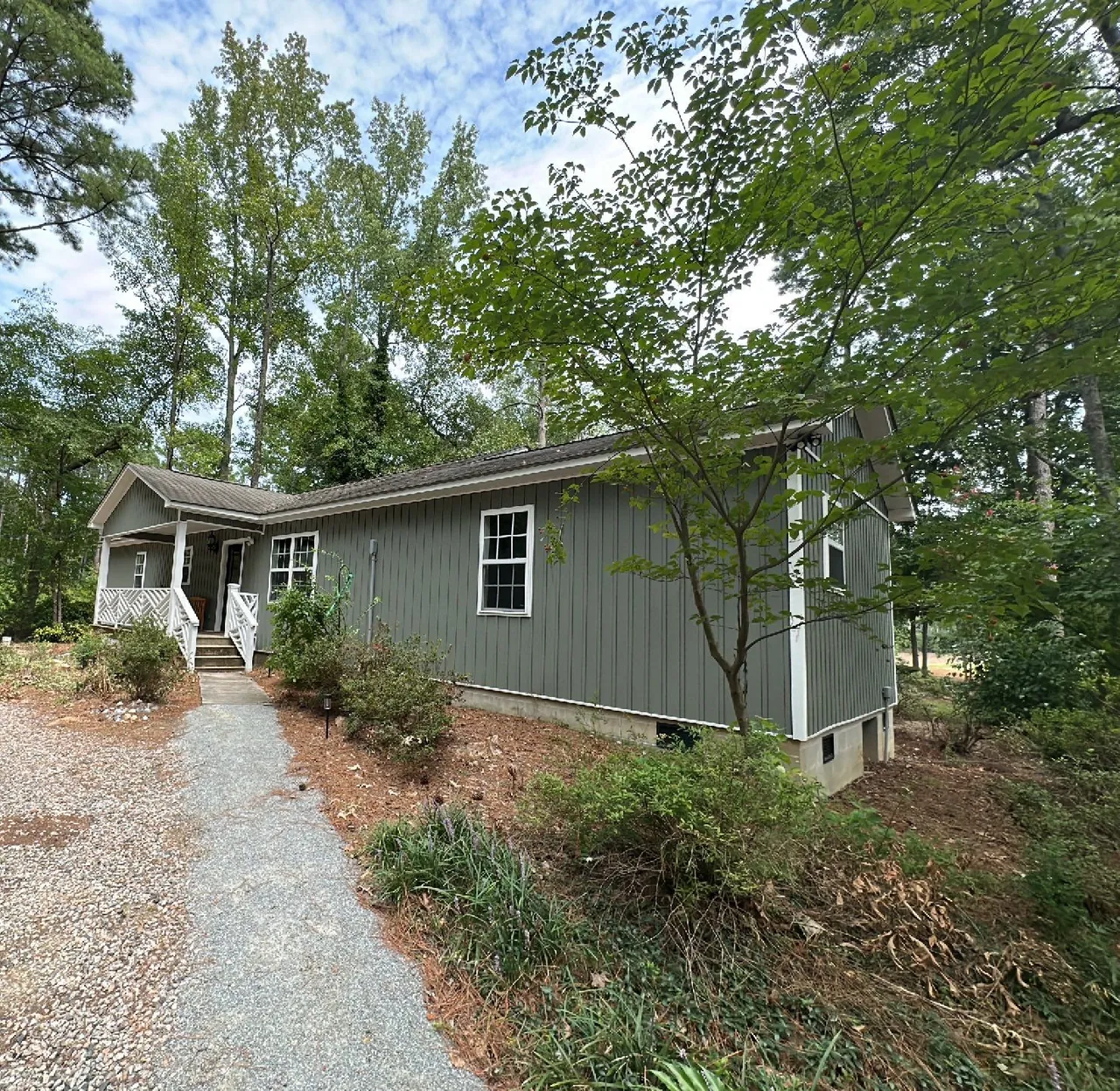 Green board-and-batten home with a covered front porch among trees in Enfield, NC, at the roof inspection