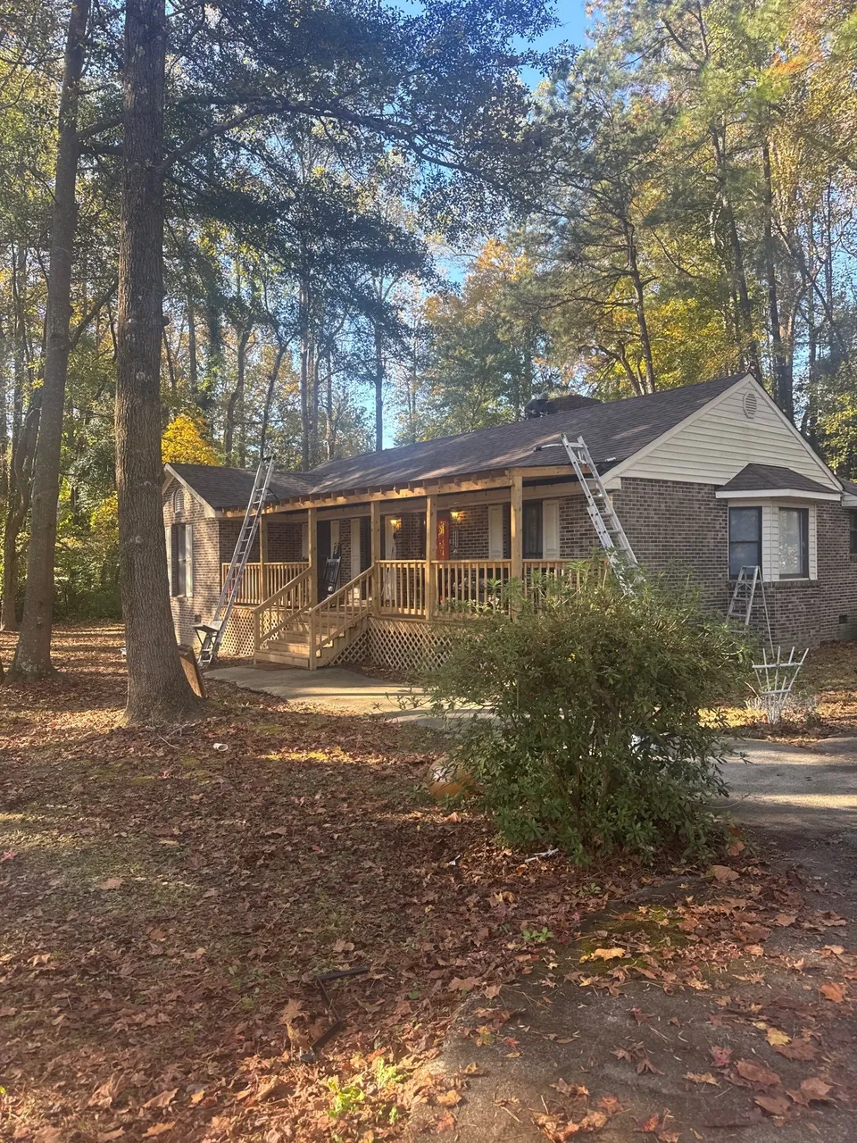 Brick ranch home with a front porch among tall trees in Roanoke Rapids, NC, with ladders up at the end of the re-roof