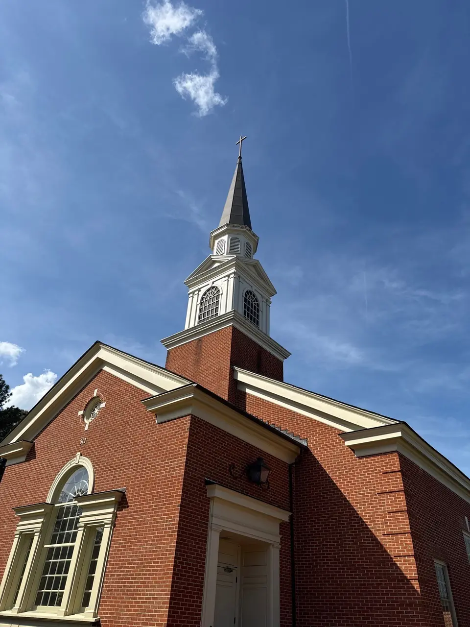 White church steeple with a cross on a red-brick tower above a church entrance in Nashville, NC