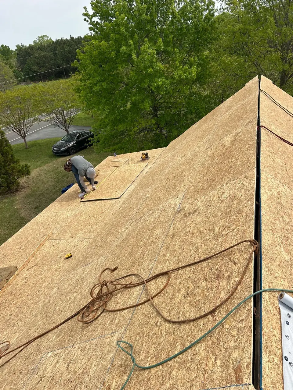 Roofer laying new OSB roof sheathing on a house in Nashville, NC, seen from the ridge
