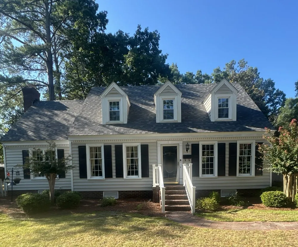 The same white Cape Cod home in Rocky Mount, NC with three dormers under a new shingle roof, late August 2026