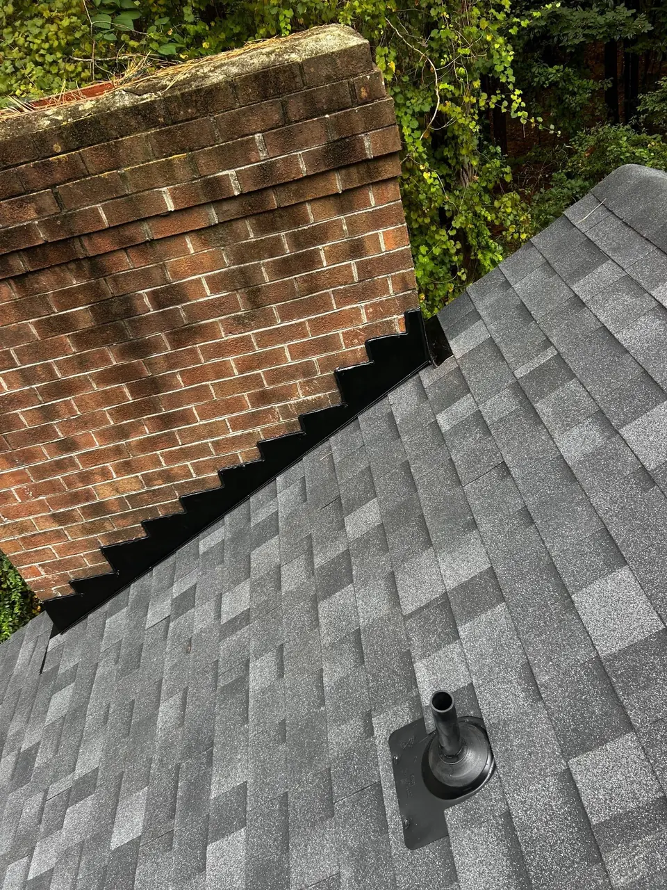 Black step flashing where new gray shingles meet a brick chimney on a Rocky Mount, NC roof