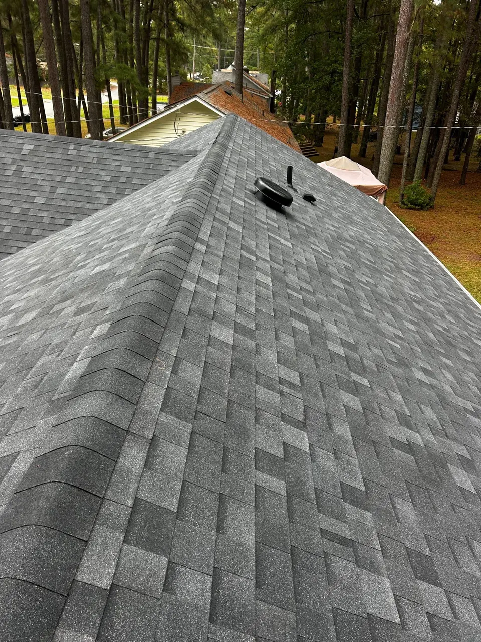 New rubber pipe boot on a plumbing vent beside a roof vent and a hip of new gray shingles in Rocky Mount, NC