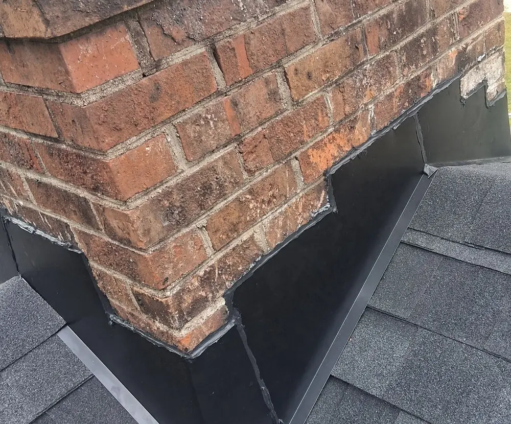 New black metal flashing stepped into the brick of a chimney and lapped over new shingles on a Rocky Mount, NC roof