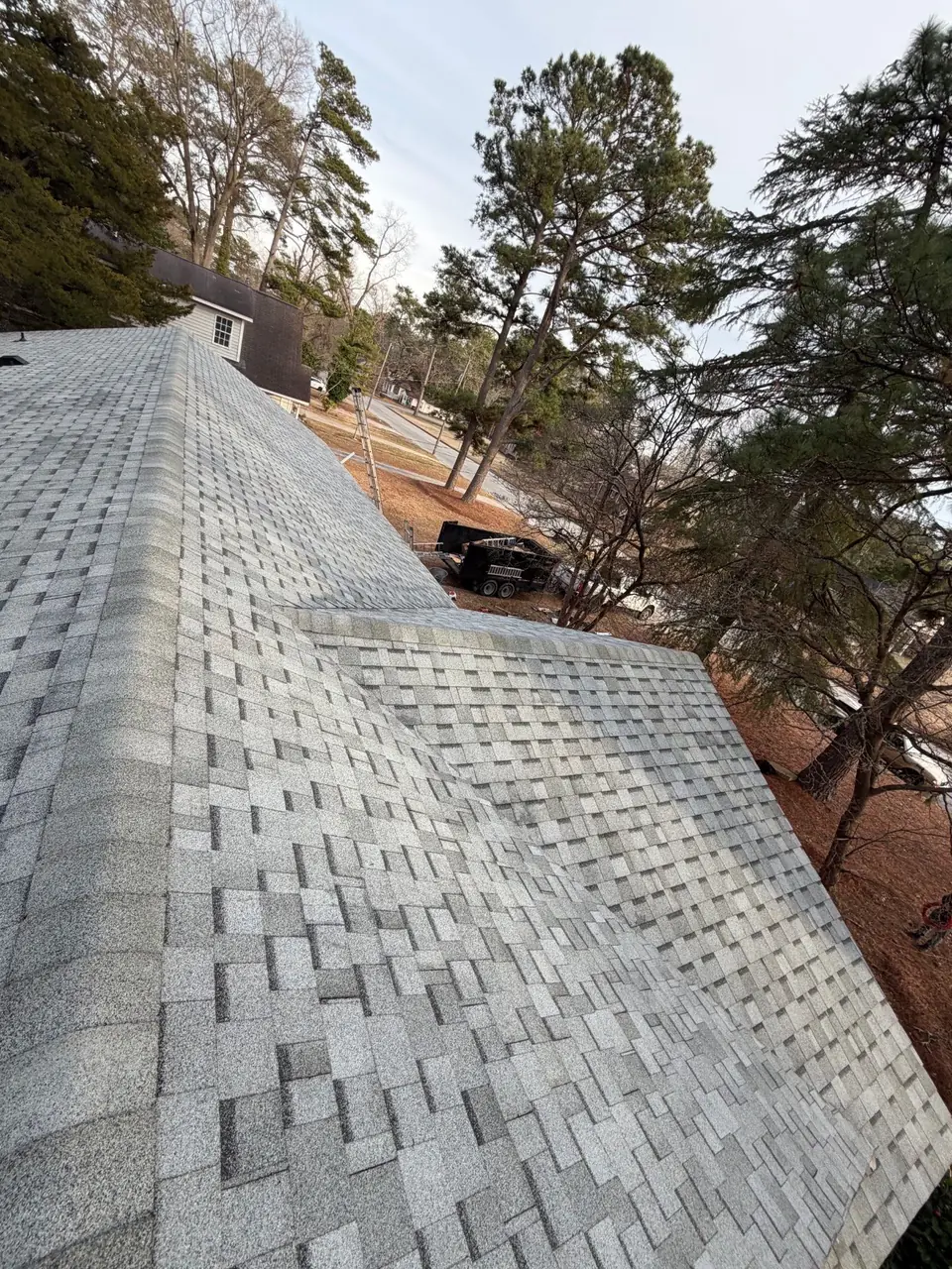 New light gray architectural shingle roof in Rocky Mount, NC, seen from the ridge with capped hips and pine trees beyond