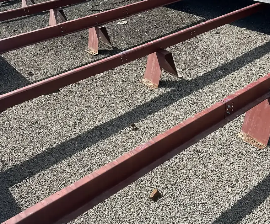 Rows of red steel framing on short supports across an old gravel-surfaced flat commercial roof in Rocky Mount, NC, ready to carry new metal panels