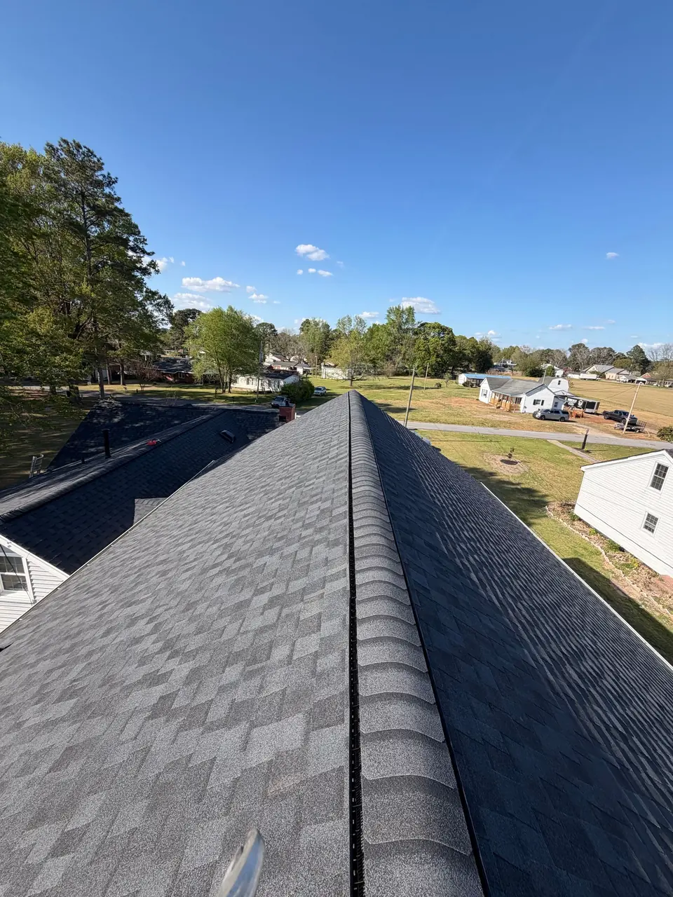 New charcoal ridge cap shingles along the peak of a roof in Macclesfield, NC, with farmland beyond