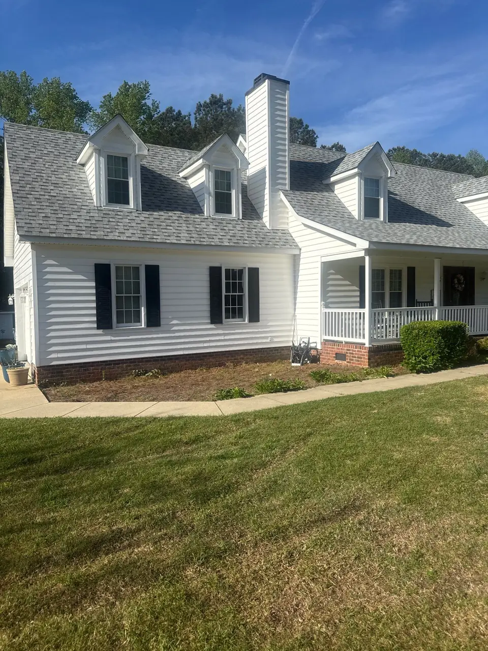 Dormers, chimney and covered porch under a new light gray shingle roof on a home in Pinetops, NC