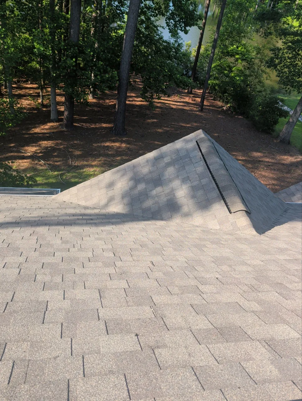 New brown-blend architectural shingles and hip caps with a ridge vent on a home in Chocowinity, NC, trees beyond