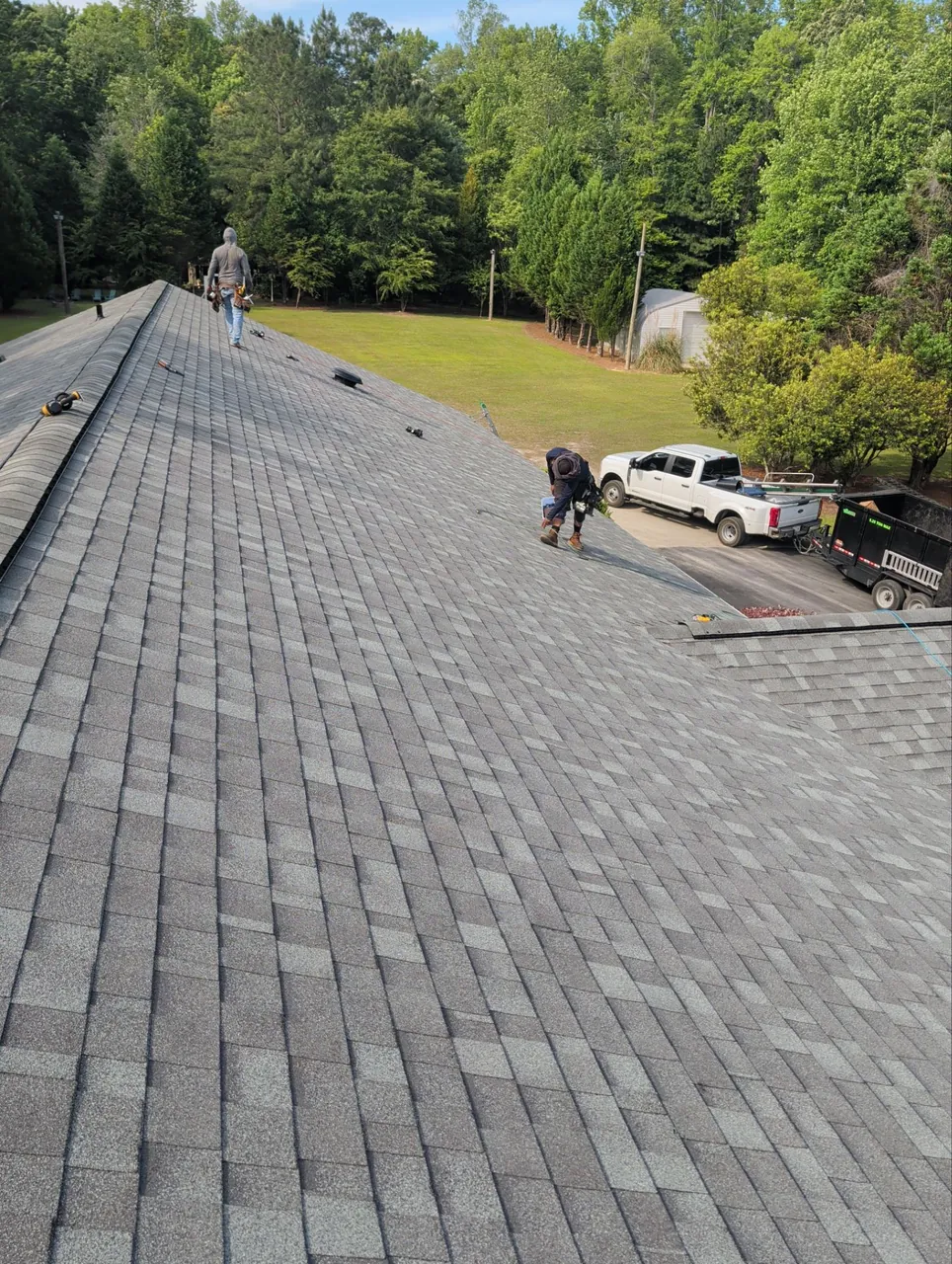 Roofers installing new gray architectural shingles along a long roof in Washington, NC