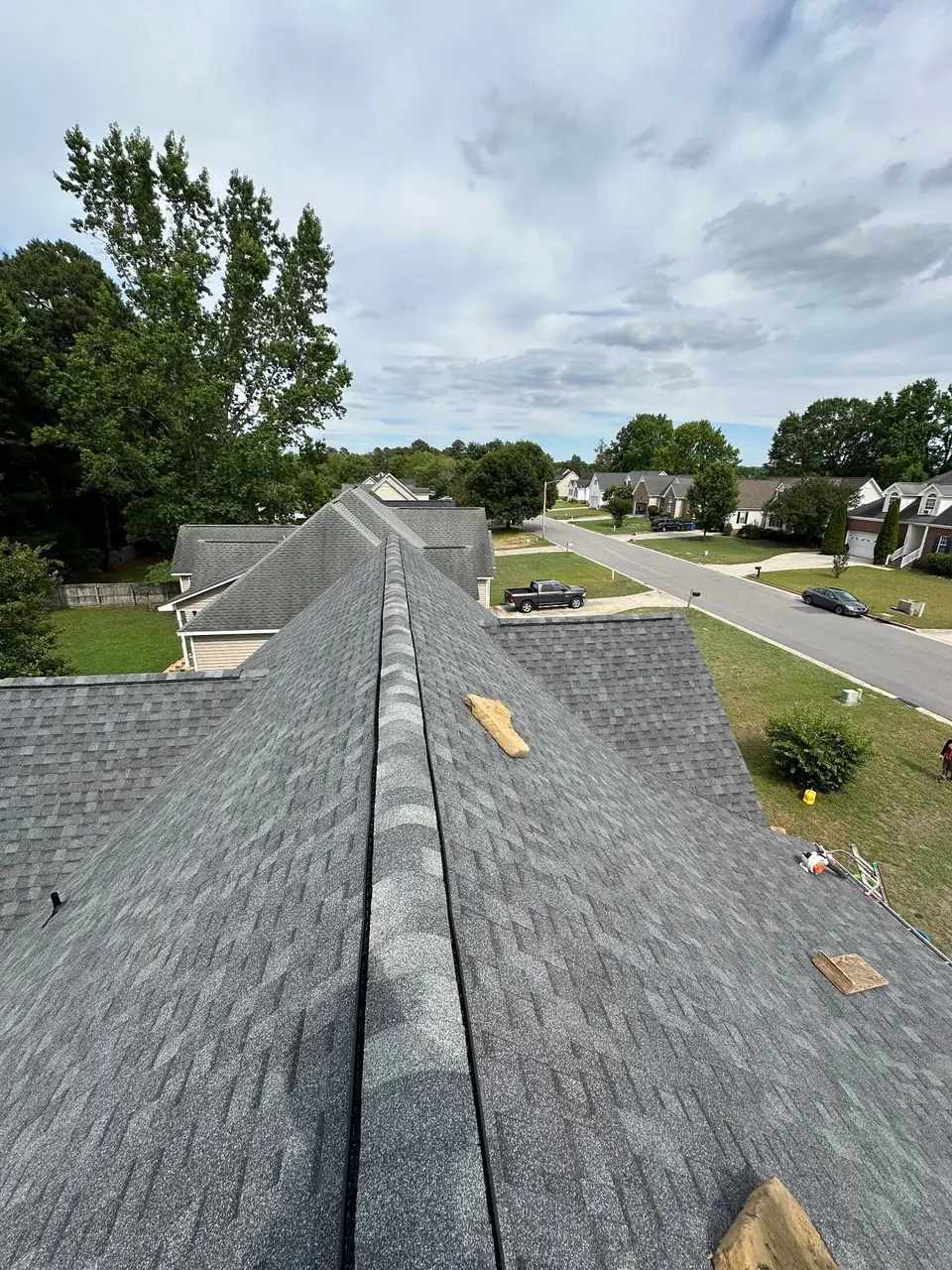 New gray architectural shingles and ridge caps on a two-story home in Wilson, NC, looking along the ridge toward the street