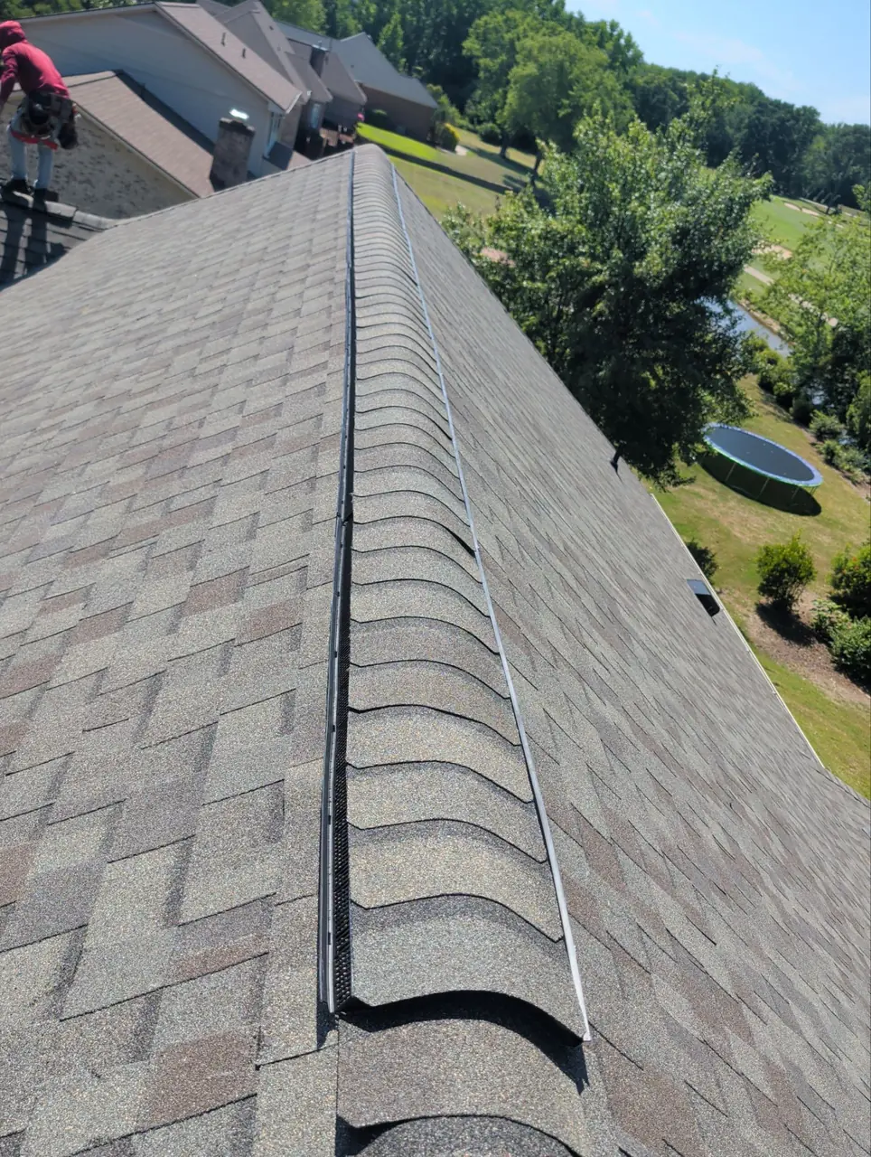Filtered ridge vent along the peak of a new brown-blend shingle roof in Wilson, NC, with cap shingles being installed over it