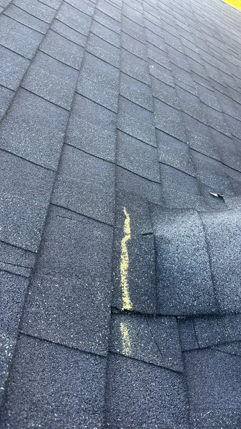 Close-up of an asphalt shingle roof where a vertical crease and lifted tab in a shingle has been outlined in bright yellow chalk during an inspection.
