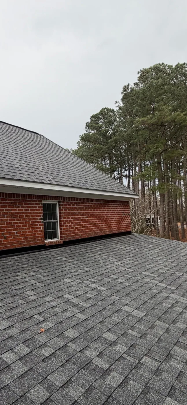 Mid-gray pewter blend architectural shingles meeting the red brick wall of a colonial home in Eastern North Carolina