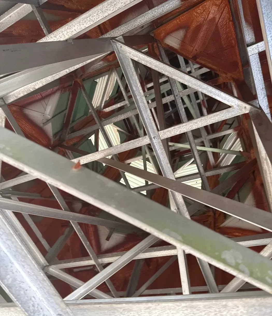 Interior view of a steeple belfry showing a lattice of aluminum structural bracing and cross-members behind the louvers.