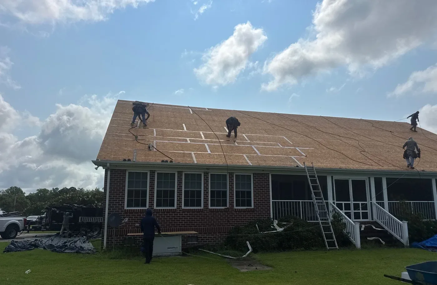 Roofers working across a roof deck where white sealing tape has been run over the horizontal panel seams and vertical butt joints.