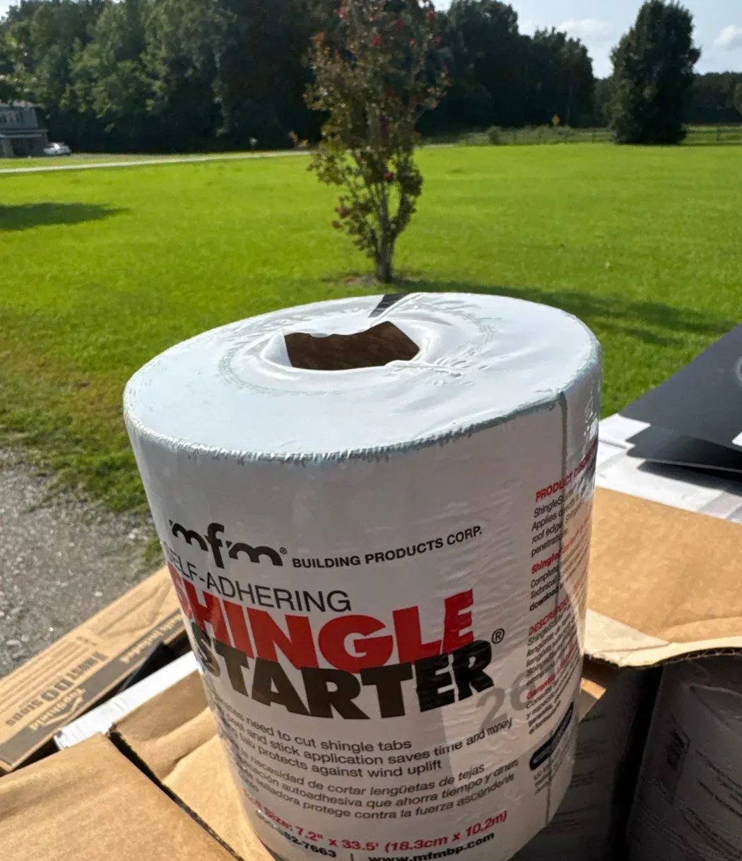 A labelled roll of MFM self-adhering shingle starter resting on its carton in the yard at the job site.