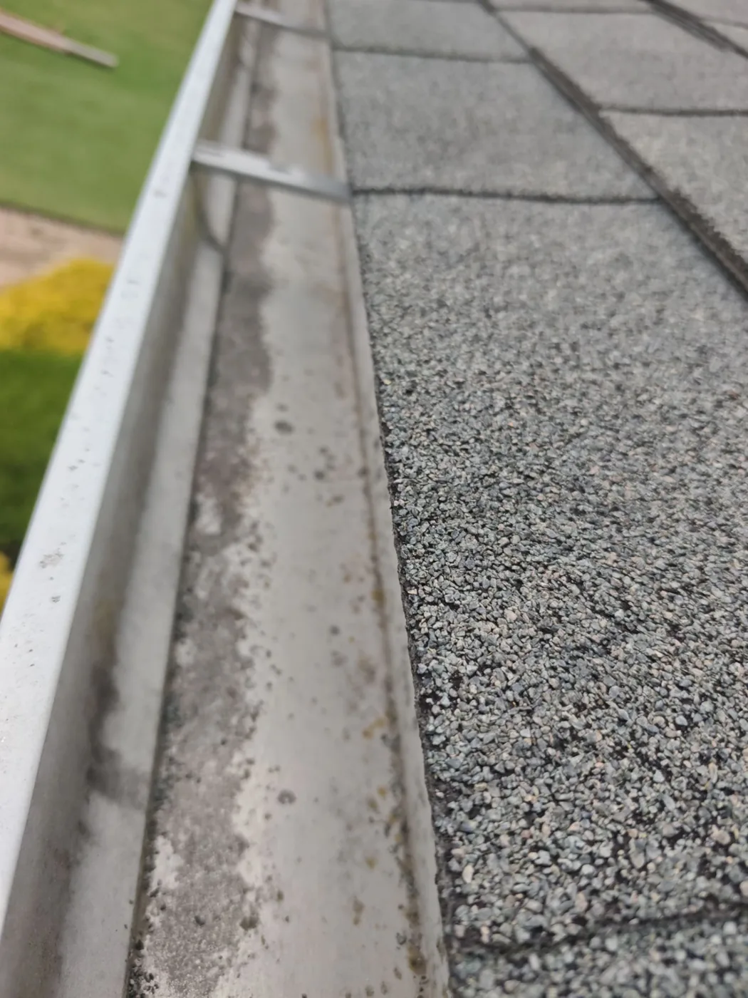A white gutter on an Eastern NC home with a heavy band of loose shingle granules collected in the trough after storm damage