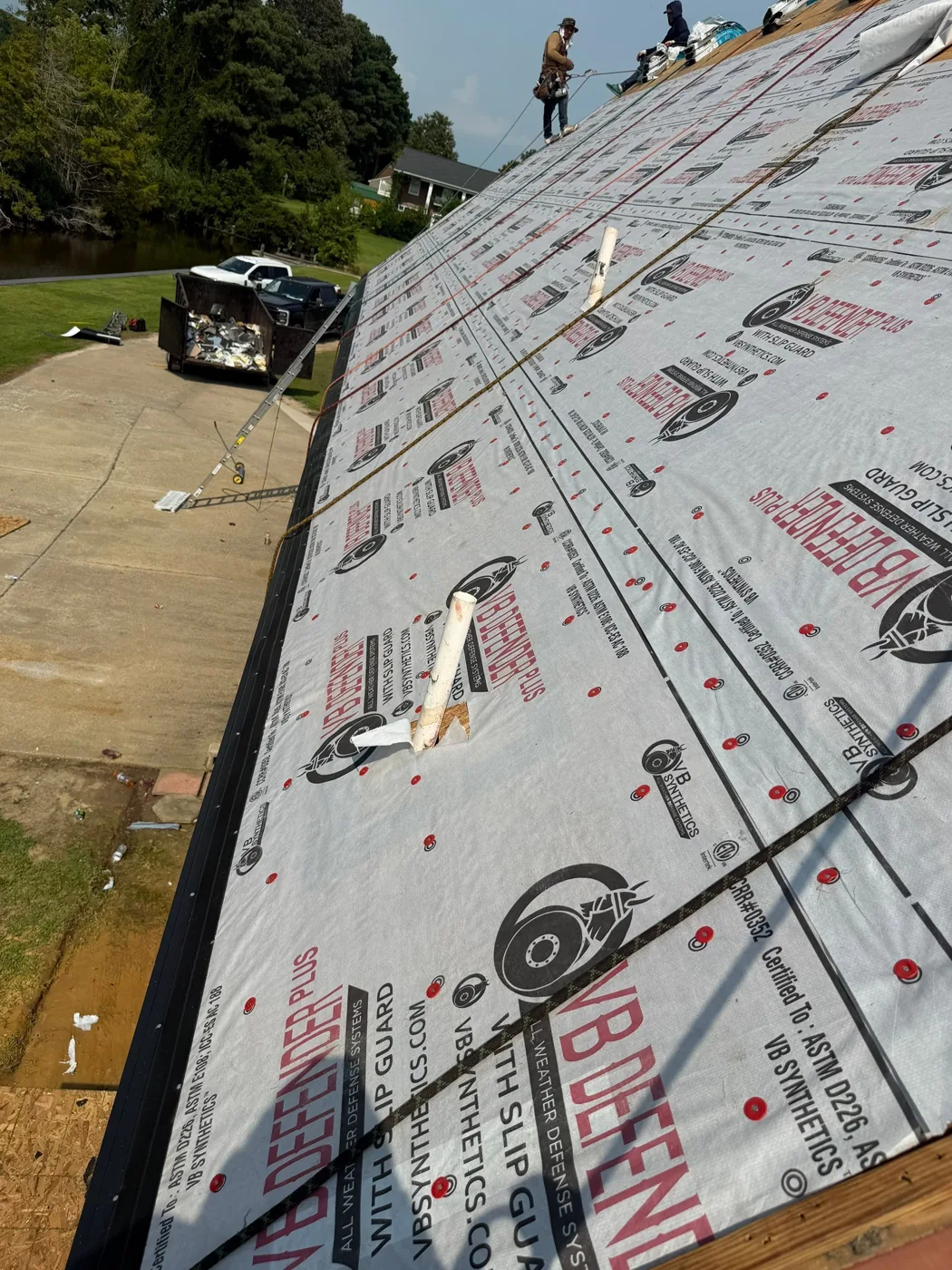 A long roof slope fully covered in printed synthetic underlayment held down by red plastic cap nails, with black drip edge fitted along the eave.