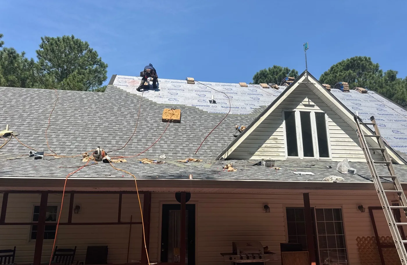 New architectural shingles being installed up the main slope over white synthetic underlayment, with bundles staged along the roof and a crew member nailing off a course near the ridge.