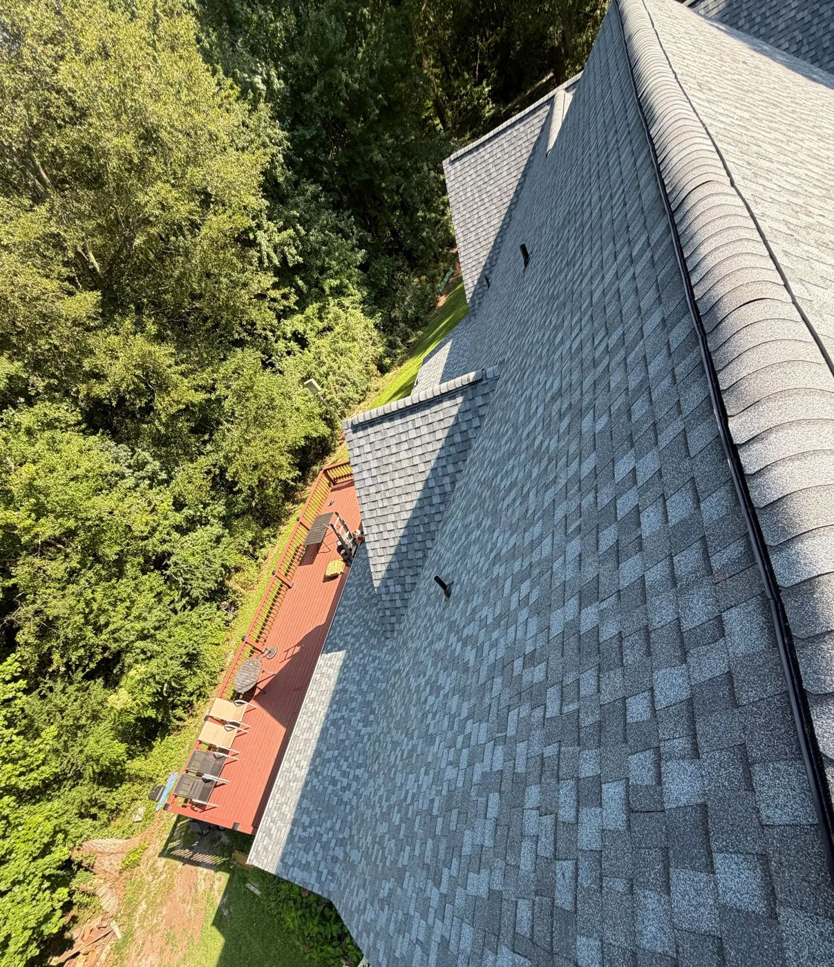 Close view along the finished roof showing straight, evenly spaced courses of grey architectural shingles running into a capped hip and ridge.