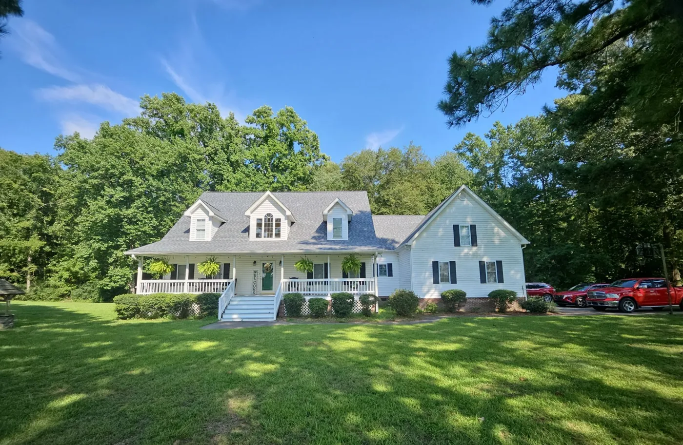 Soft gray blend architectural shingle roof on a white farmhouse-style home with a wraparound porch in Eastern North Carolina