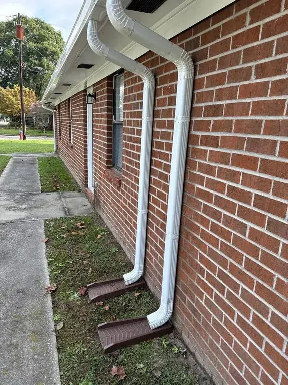 Two white downspouts on a brick wall ending in brown splash blocks on the ground