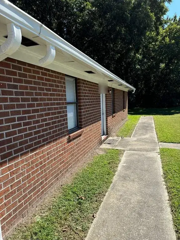 White seamless gutter running along the eave of a brick building with two downspout elbows coming off it