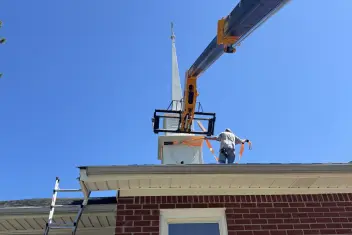 Steeple being set onto a brick church roof from a telehandler boom